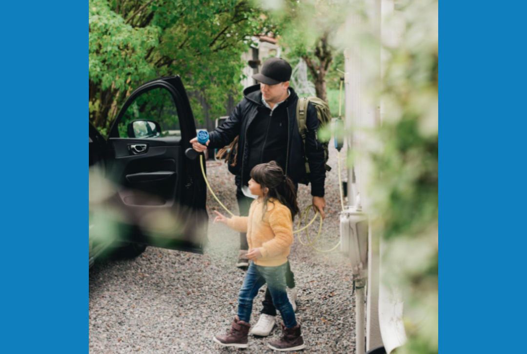 image Man holding charging cord next to house and vehicle while child stands nearby